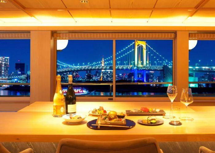 The interior of our luxury Tokyo Bay cruise, showing bottles of wine and premium dishes in front of the Rainbow Bridge.